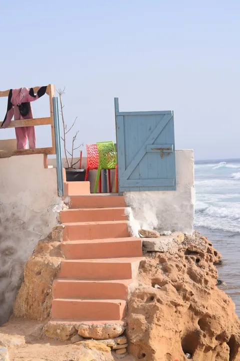 Un escalier ocre mène à une porte bleue au bord de l’océan.