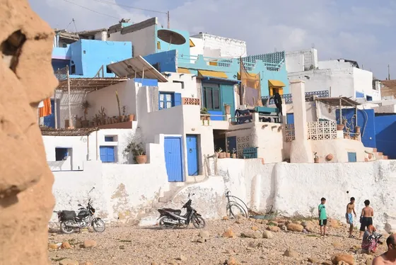 Maisons blanches et bleues d’un village côtier, au-dessus d’une plage.