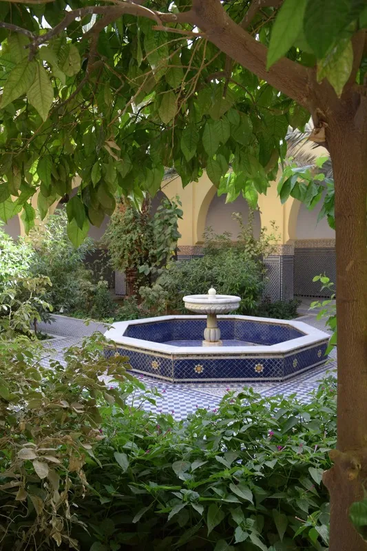 Une fontaine de zellige au cœur d’un jardin ombragé.