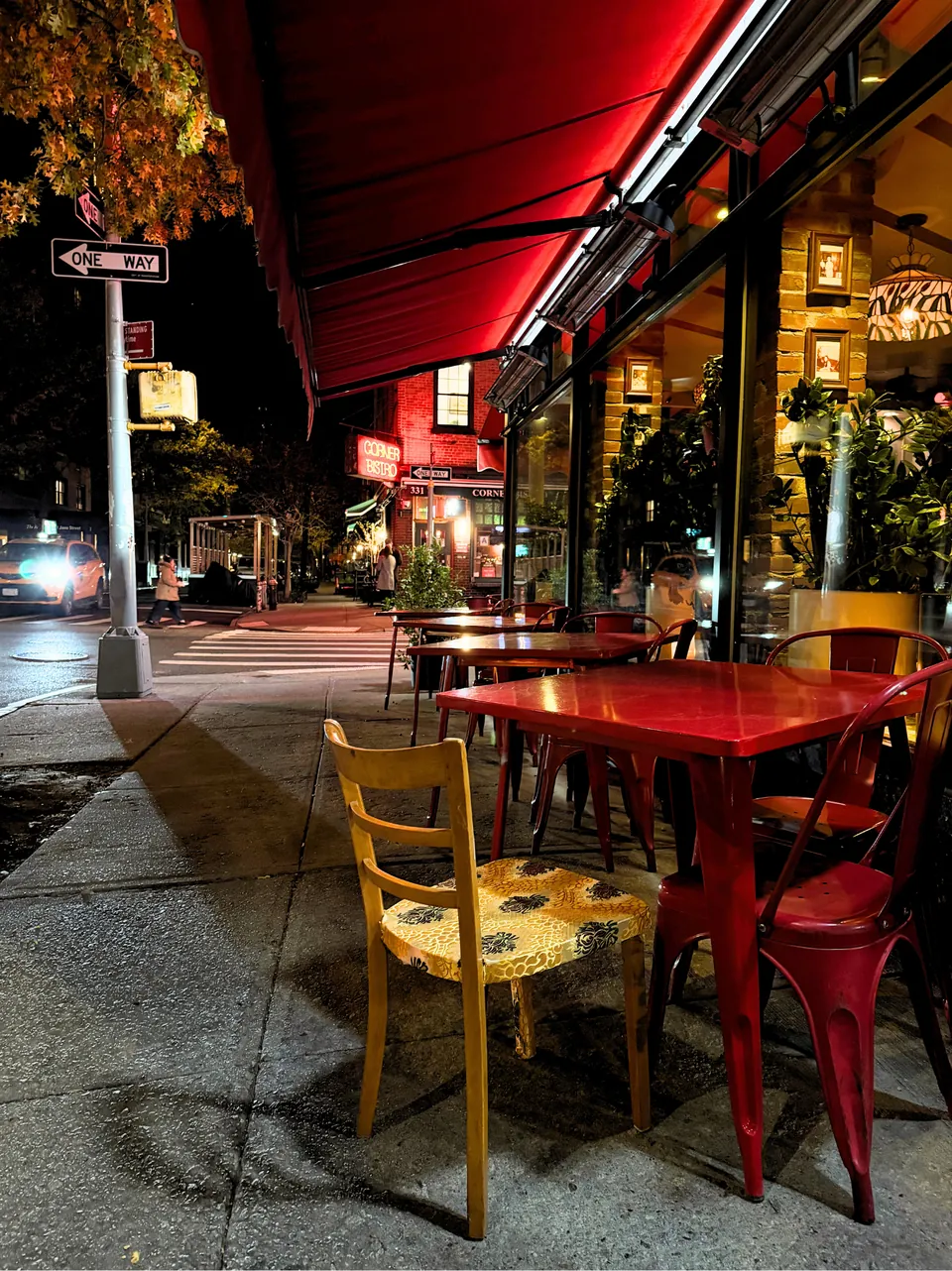 La même chaise, la nuit, sur une terrasse de la ville parmi des chaises et des tables industrielles rouges.