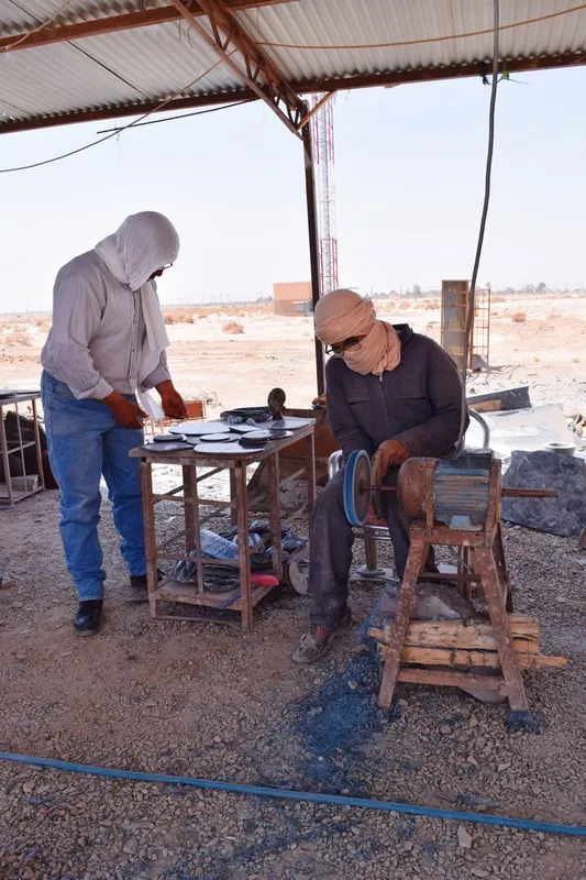 Deux artisans au travail sous un abri de tôle, dans un paysage aride.