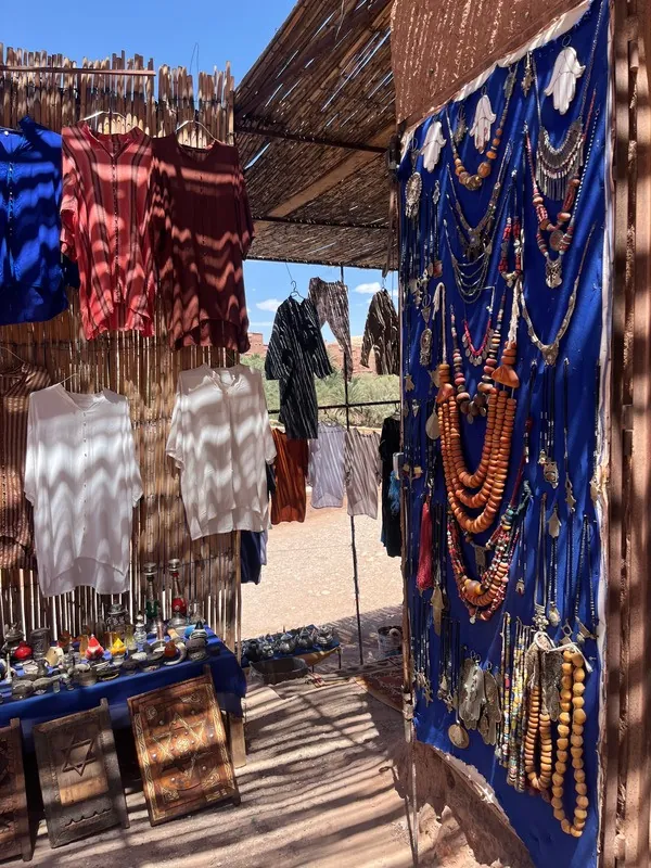 Un étal de marché : écheveaux de laine teinte, tissus bleus et colliers de perles.